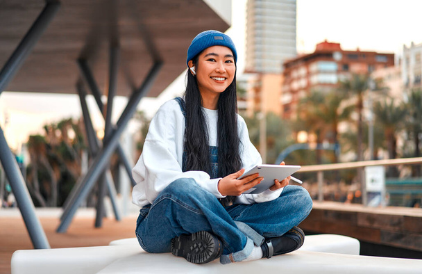 Mulher asiática bonito em um chapéu com um tablet na rua. Desenho em um tablet gráfico. Freelancing e ganhar on-line. - Foto, Imagem