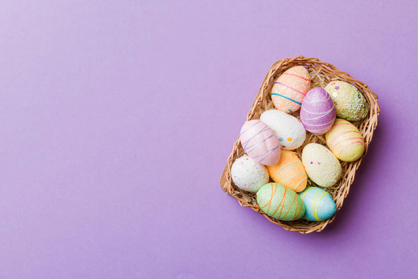 Colorful Easter eggs in wicker basket against colored background, closeup. top view with copy space. - Foto, Imagem