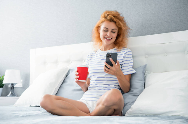 glad woman with coffee surfing internet on phone. woman surfing internet at home with phone. internet surfing at home of woman. - Foto, Imagem