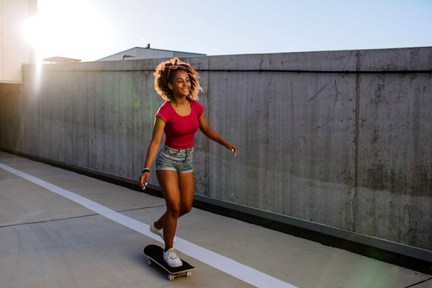 Multiracial teenage girl riding skateboard in front of concrete wall, balancing. Side view. - Фото, изображение