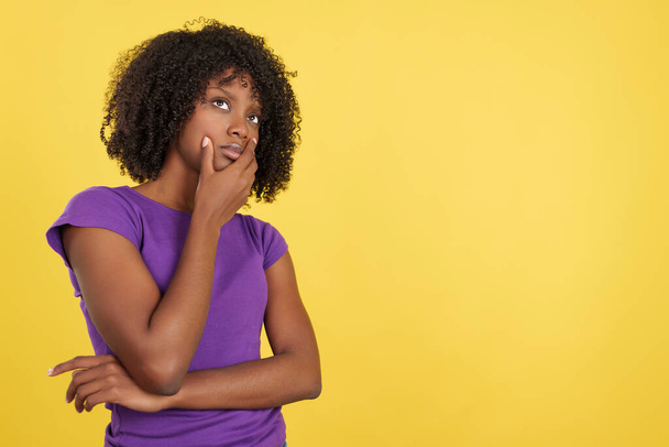 Жінка з афро волоссям стоїть з продуманим виразом в студії з жовтим тлом
 - Фото, зображення