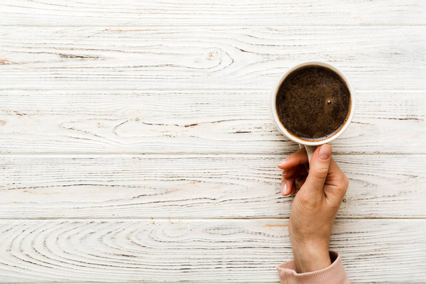 Minimalistic style woman hand holding a cup of coffee on Colored background. Flat lay, top view cappuccino cup. Empty place for text, copy space. Coffee addiction. Top view, flat lay. - Φωτογραφία, εικόνα