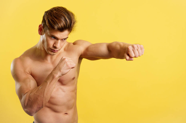 Sterke man doet schaduwboksen met kale romp in studio met gele achtergrond - Foto, afbeelding