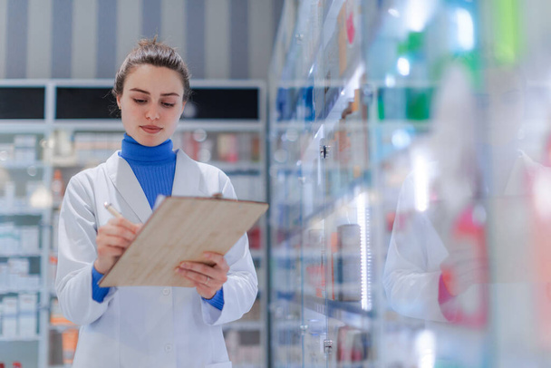 Young pharmacist checking medicine stock in a pharmacy. - 写真・画像