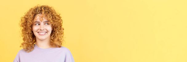 Imagen de estudio panorámica con fondo amarillo de una mujer de belleza feliz con el pelo rizado mirando a un lado - Foto, Imagen