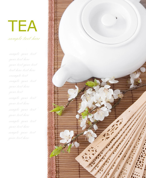 Травяной чай (завтрак с чайником, чашкой и цветком цветов на бамбуковом коврике изолированы на белом с образцом текста
 ) - Фото, изображение