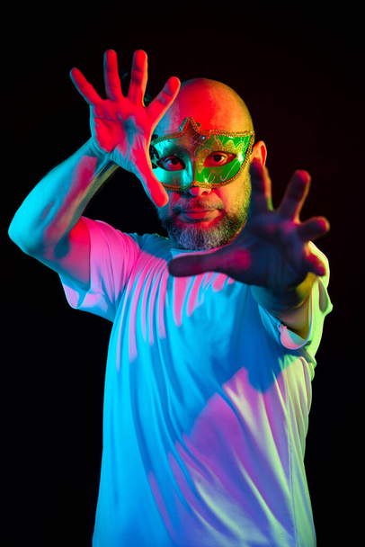 Man portrait, bald, wearing carnival mask. Making gestures with your hands. Isolated in the black background. - Fotoğraf, Görsel