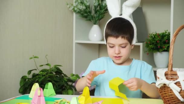 Ragazzo in età prescolare con testa di ronzino orecchie di coniglio fa mestieri pasquali, figurine origami di conigli e cestini di carta. - Filmati, video