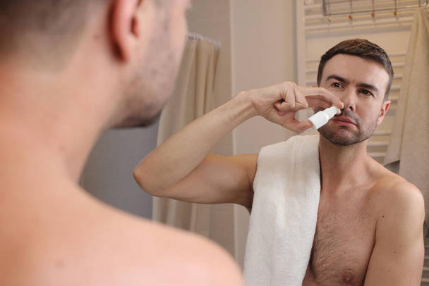 Porträt eines hübschen jungen Mannes, der im Badezimmer Nase vor Spiegel sprüht - Foto, Bild