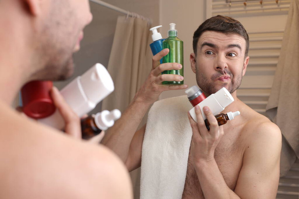 retrato de belo jovem com garrafa de suprimentos de higiene na frente do espelho no banheiro - Foto, Imagem