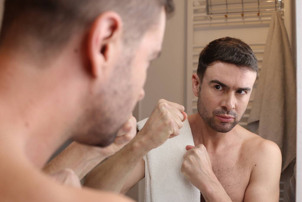 portret przystojnego agresywnego młodego mężczyzny przed lustrem w łazience - Zdjęcie, obraz