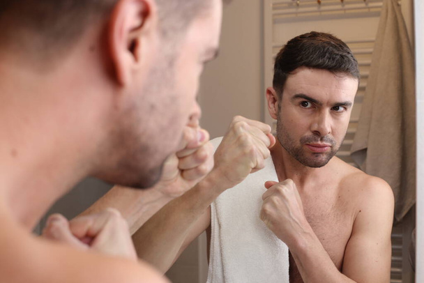 portrait of handsome aggressive young man in front of mirror in bathroom - Photo, Image