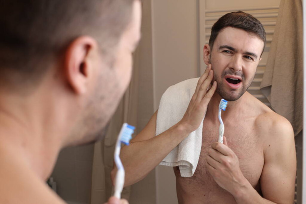retrato de joven guapo con cepillo de dientes y toalla delante del espejo en el baño - Foto, imagen
