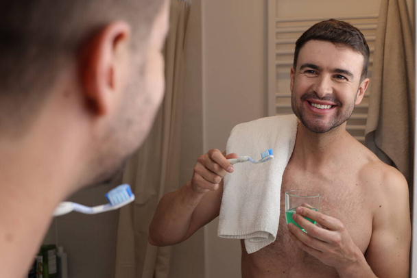 muotokuva komea nuori mies hammasharja ja pyyhe edessä peili kylpyhuoneessa - Valokuva, kuva