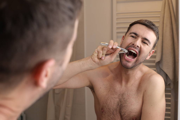 retrato de un joven guapo sacando los dientes delante del espejo en el baño - Foto, imagen