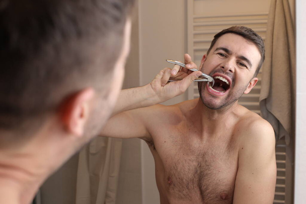 portret van knappe jonge man trekken zijn tanden in de voorkant van spiegel in de badkamer - Foto, afbeelding