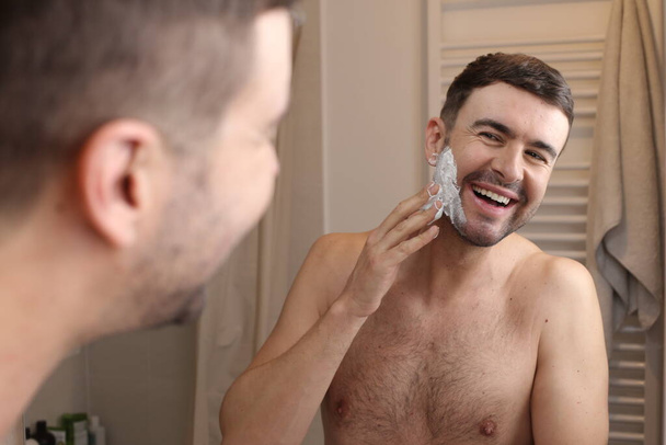 portret przystojnego młodego mężczyzny nakładającego piankę do golenia przed lustrem w łazience - Zdjęcie, obraz