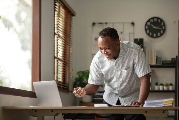 Портрет красивого африканского чернокожего молодого бизнесмена, работающего на ноутбуке в офисе.. - Фото, изображение
