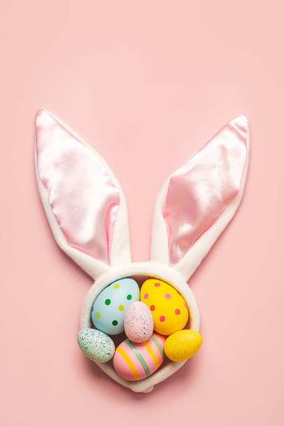 Feliz Pascua. Huevos pintados de Pascua coloridos en orejas de conejo blanco con espacio de copia para texto sobre fondo rosa - Foto, imagen