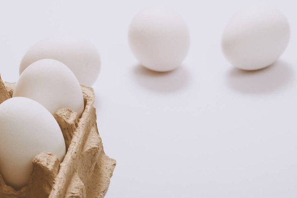Weiße Eier auf hellem Hintergrund und in braunem Eierfach. Selektiver Fokus. Konzeptszene. - Foto, Bild