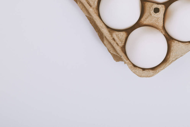 Weiße Eier in braunem Eierfach auf hellem Hintergrund. Selektiver Fokus. Konzeptszene. Ansicht von oben.  - Foto, Bild