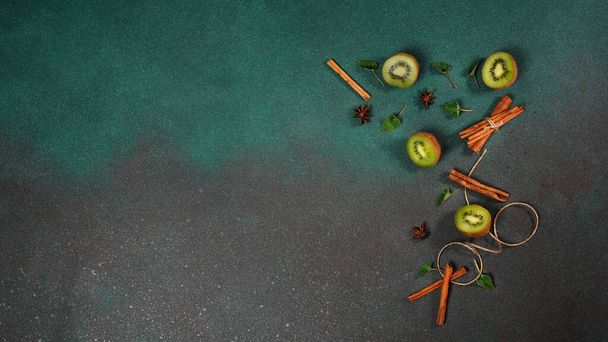 Kawałki świeżego, soczystego Kiwi na zielonym tle. Ozdobiony paluszkami cynamonowymi, niegrzecznym, liśćmi mięty. Owocowe dekorowane tło. Widok z góry - Zdjęcie, obraz