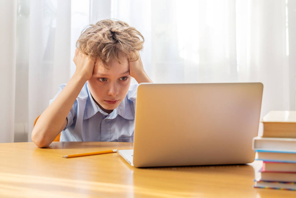 Bedachtzame schooljongen studeren online op laptop aan bureau met boeken en briefpapier - Foto, afbeelding