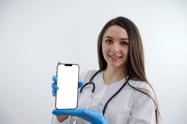 Portrait of medical doctor woman with stethoscope and phone in hands. Isolated on white background. High quality photo - Zdjęcie, obraz