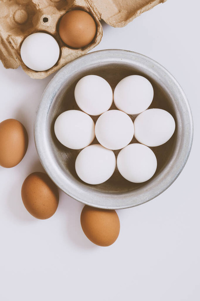 Brown eggs on bright background. White eggs in metal bowl and eggs in brown tray on bright background. Close up, selective focus.Concept scene. Top view.  - Photo, Image