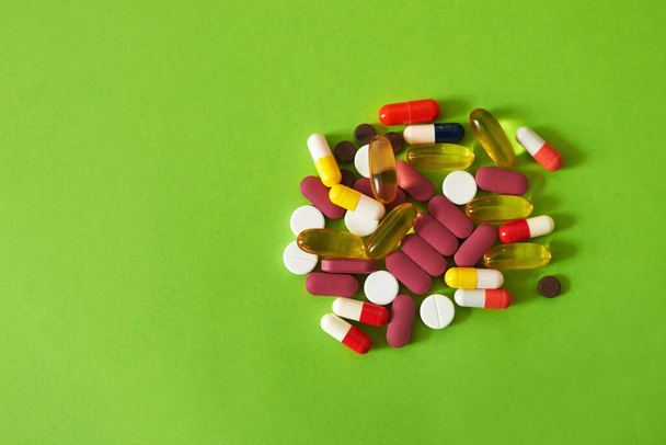 Small in size, big on health. Studio shot of a pile of different tablets against a green background - Zdjęcie, obraz