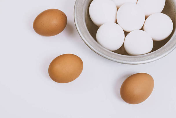 Ovos castanhos sobre fundo brilhante e ovos brancos em tigela de metal. Fechar, foco seletivo. Cena de conceito.  - Foto, Imagem