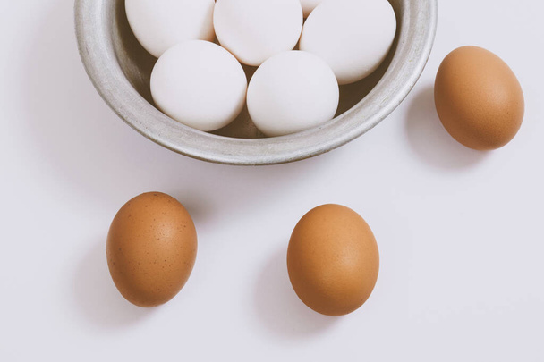 Braune Eier auf hellem Hintergrund und weiße Eier in Metallschüssel. Nahaufnahme, selektiver Fokus. Konzeptszene.  - Foto, Bild