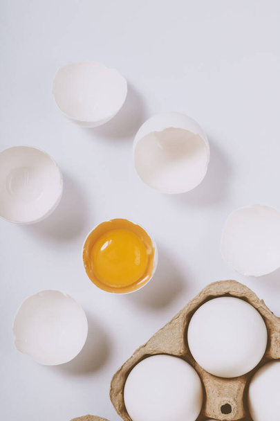 Тріснуте яйце наполовину з жовтком всередині біля яєчного лотка з яйцями на яскравому фоні. Вибірковий фокус. Концепція сцени. Вид зверху - Фото, зображення