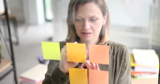 Eine Geschäftsfrau schreibt in Großaufnahme auf einen klebrigen Zettel an einer Glaswand im Büro. Organisation von unternehmerischen Aufgaben - Filmmaterial, Video