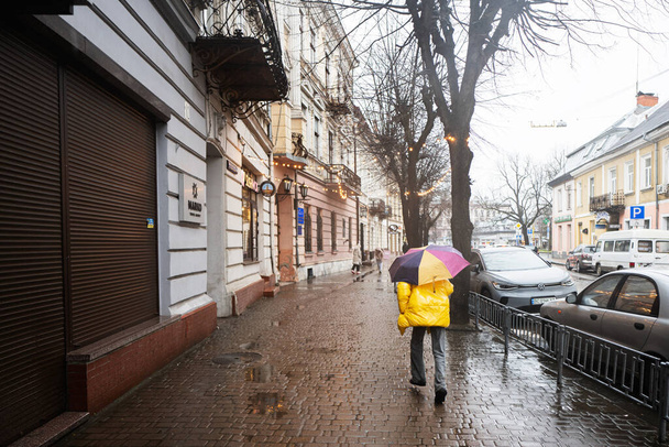 Ivano-Frankivsk, Ukraine - March, 2023: Woman in yellow with umbrella walking in rain street. - Photo, Image