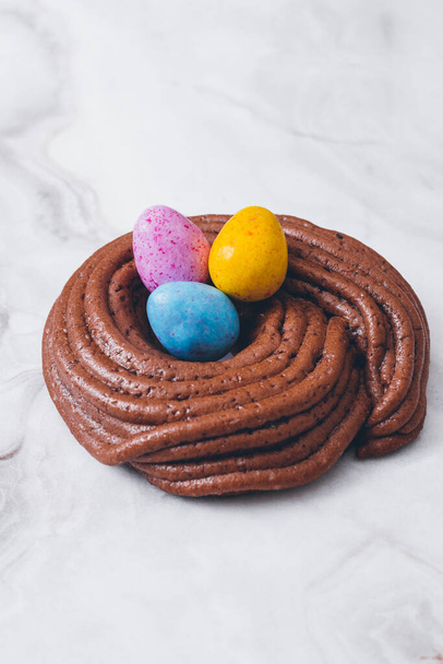 Easter nest cookie. Nest shape cookie with multicolored easter eggs in the center. Easter eggs covered by colorful candy shell.  Baked chocolate nest cookie. - Fotó, kép