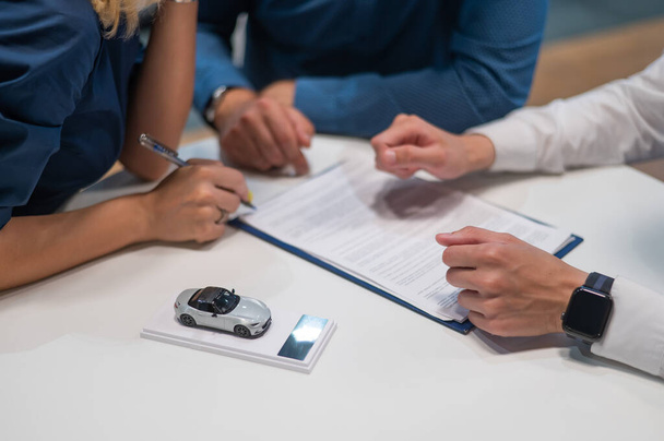 Close-up of the couples hands signing a contract to buy a car salon - Foto, imagen
