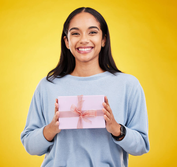 Happy woman, portrait and gift box in a studio with a smile from surprise present for birthday. Giveaway prize, isolated and yellow background of a young female student feeling positive and cheerful. - Fotografie, Obrázek