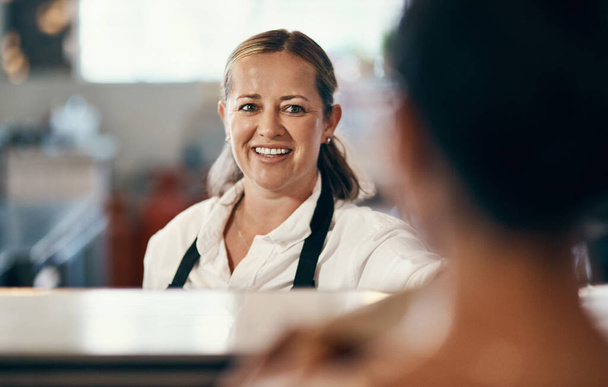 Een vriendelijke glimlach spreekt boekdelen. een volwassen barista serveert een klant in een café - Foto, afbeelding