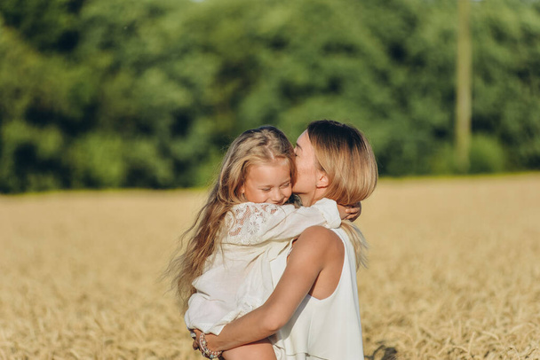 Cultivando trigo. Seguridad alimentaria. Una mujer sostiene a su hijita en sus brazos y se para en un campo de trigo en verano. - Foto, imagen