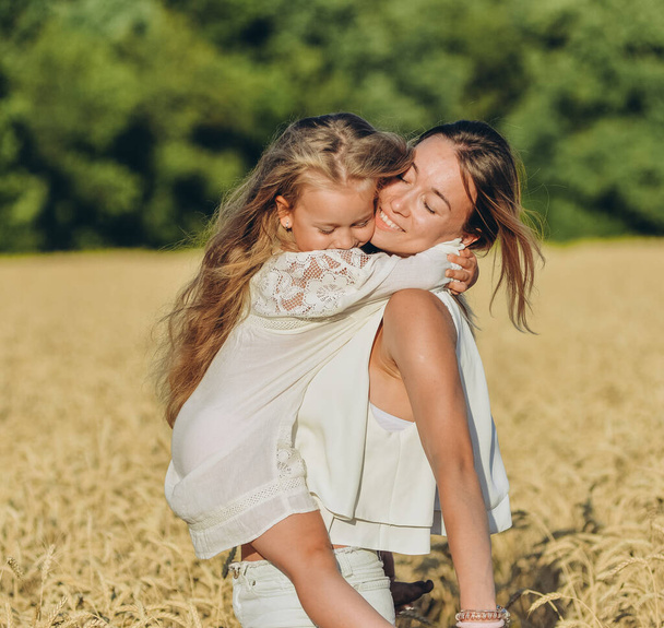 Growing wheat. Food security. A woman holds her little daughter in her arms and stands in a wheat field in summer. - 写真・画像