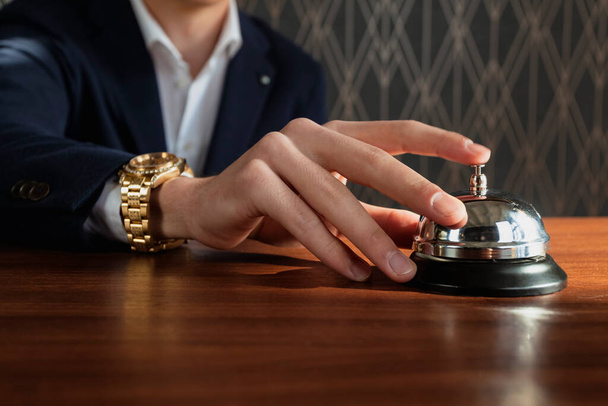 Close-up of a man in a formal dark blue suit and with golden watches is reaching his hand to a Service Bell, Call Bell, Desk Bell. - Foto, Bild