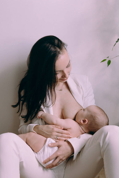 Anne yeni doğmuş bir bebeği besler, bebek bezli bir kızı kollarına alır, anne sarılır ve öper ve bebek gülümser.. - Fotoğraf, Görsel