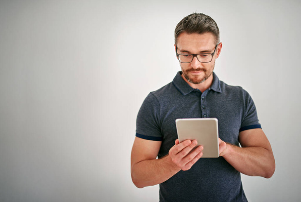 Rimanere connessi con la tecnologia touchscreen. un uomo che usa un tablet digitale su uno sfondo grigio - Foto, immagini