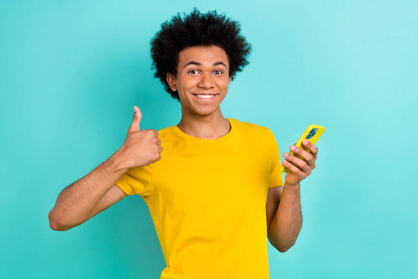 Photo de satisfait beau gars afro coiffure habillé t-shirt jaune montrant comme beau travail isolé sur fond de couleur turquoise. - Photo, image