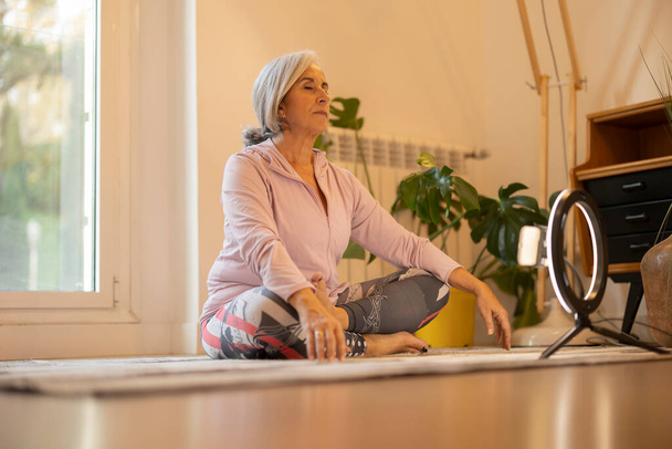 volwassen vrouw geven online yoga klasse van huis, vrij senior vrouw met grijs haar doen sport om te zorgen voor haar gezondheid - Foto, afbeelding