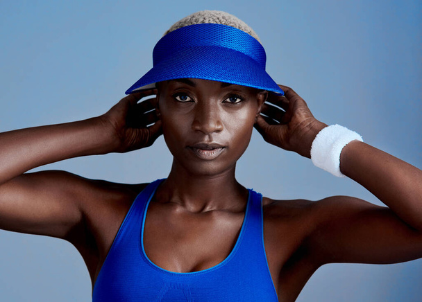 I make a workout look good. Studio shot of a sporty young woman wearing a visor while posing against a blue background - Foto, Imagen