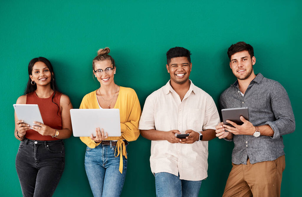 As business grows, so do our connections. Portrait of a group of young designers using digital devices while standing together against a green background - Photo, image