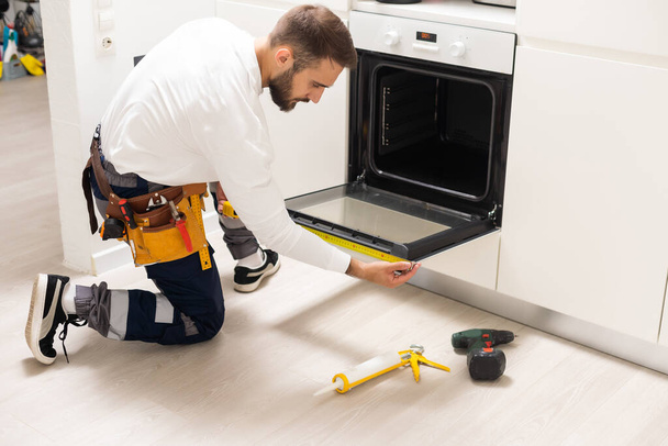 repairman examining oven with screwdriver in kitchen with tool case. - Fotoğraf, Görsel