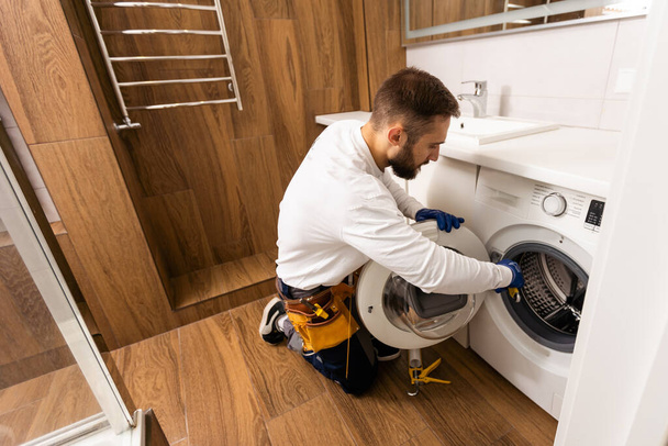 Klempner in Overalls mit Werkzeug repariert Waschmaschine im Haus - Foto, Bild